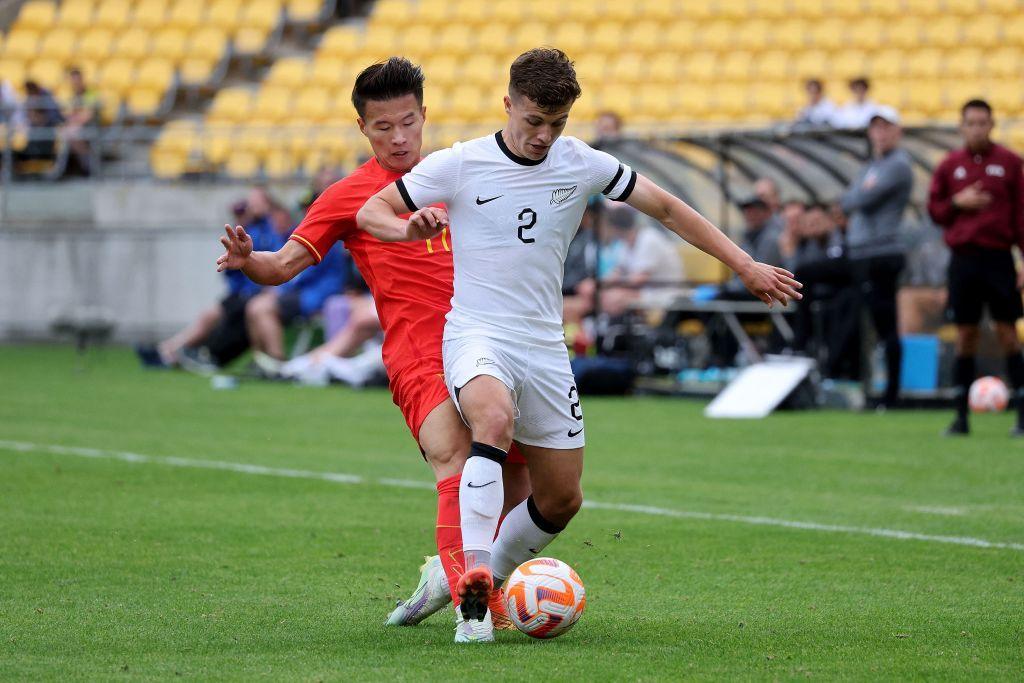 Footballer Callan Elliot in a white strip of New Zealand defends the ball from a Chinese player during an international match