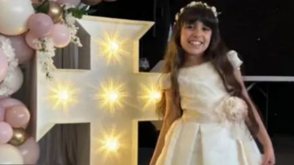 Alice da Silva Aguiar smiles at the camera while wearing her white Communion dress.