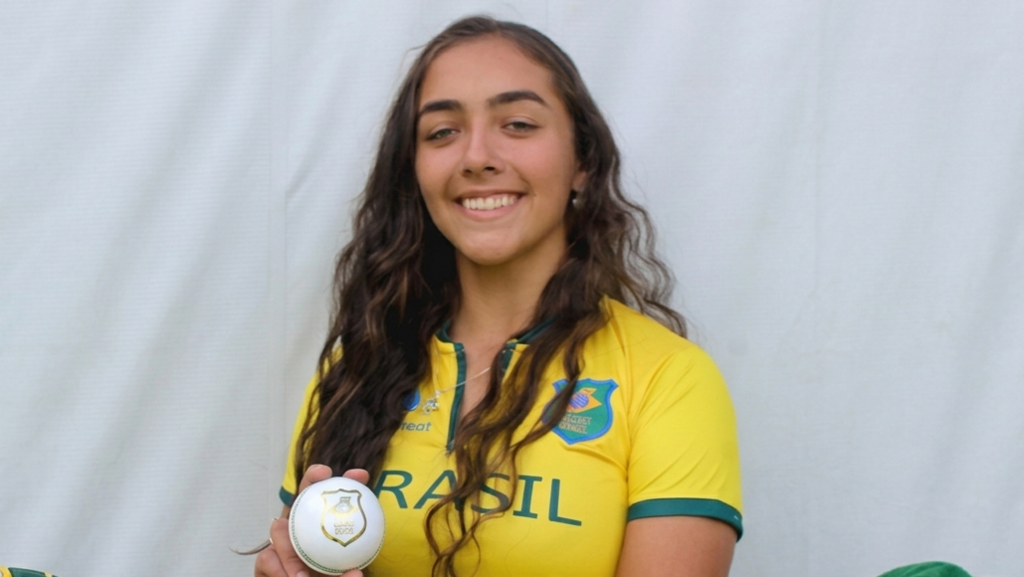 Laura Cardoso holding a white ball while wearing a Brazil cricket kit