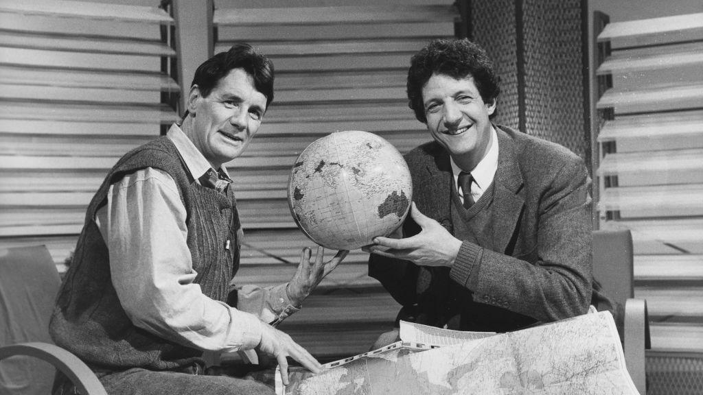 A black and white photo of Chris Serle and Michael Palin inspecting a map and globe