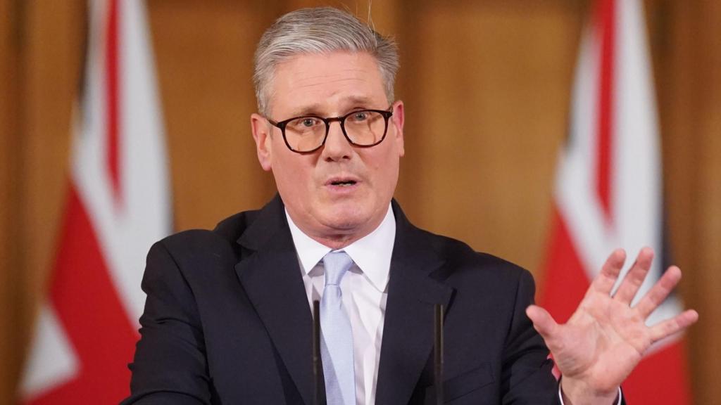 Starmer gestures with his hand with union flags in the background