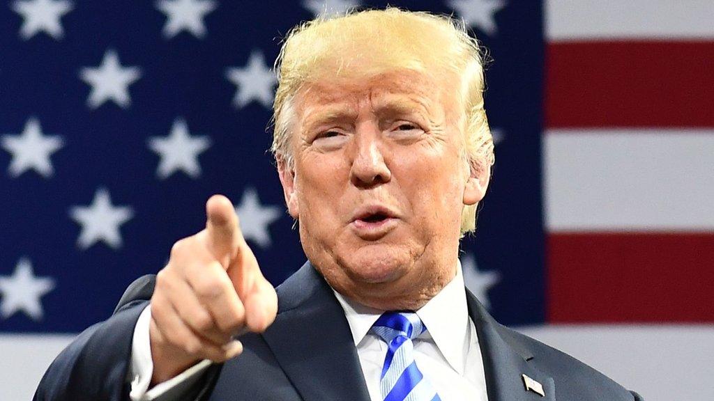 Donald Trump standing in front of the US flag at a rally