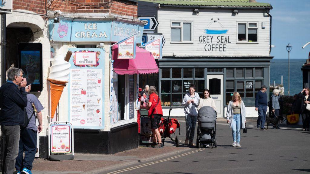 People walk along a street and pass an ice cream parlour