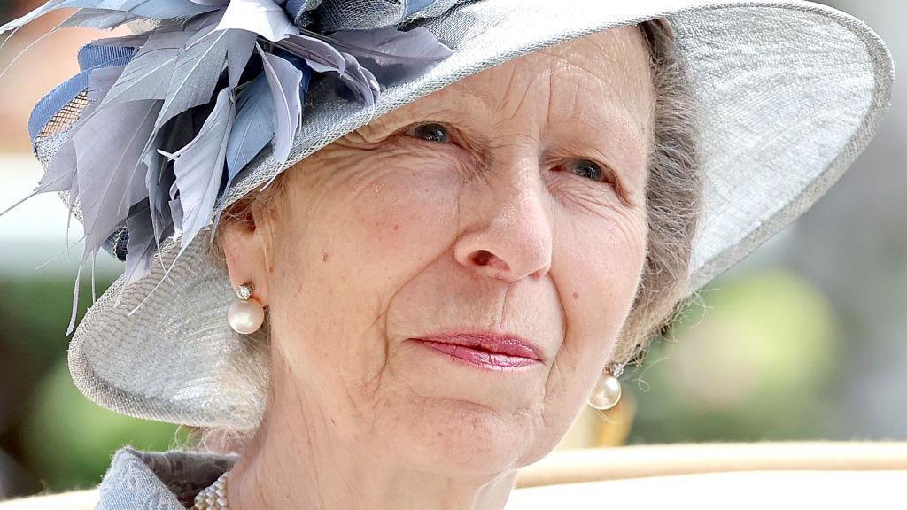 The Princess Royal, Princess Anne, in a blueish-grey hat with decorative leaves in the same colour and large pearl earrings