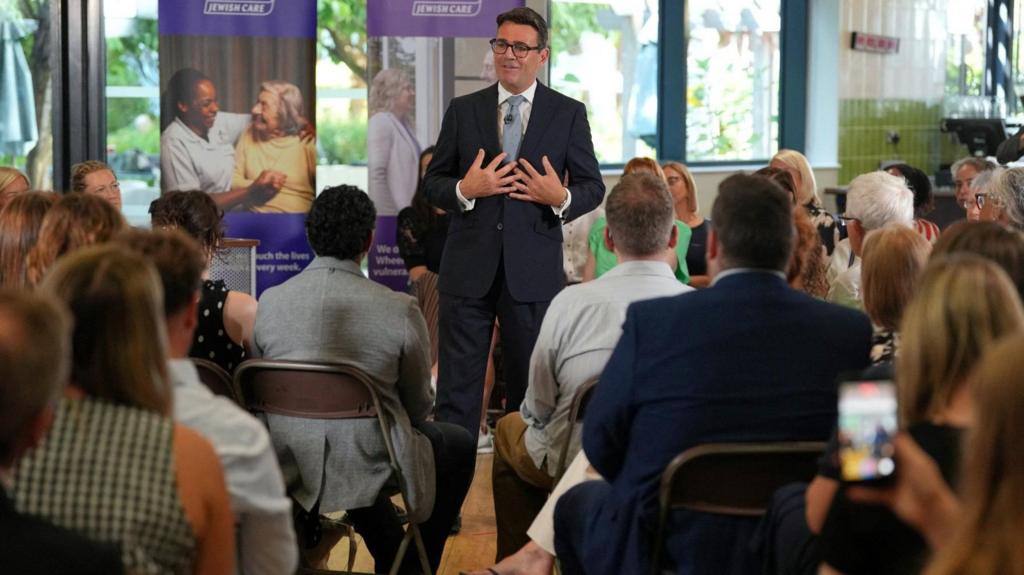 Burnham gestures with his hands while delivering a speech in a care home 