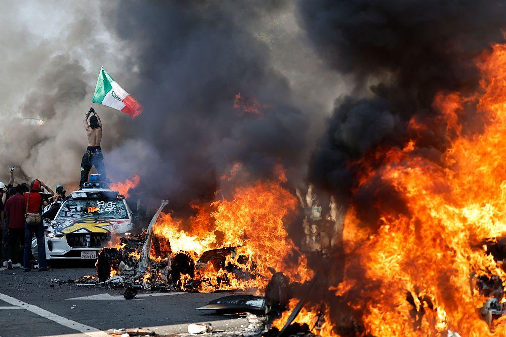 A protestor holds up a Mexican flag as burning cars line the street in Los Angeles, California, on 8 June 2025 