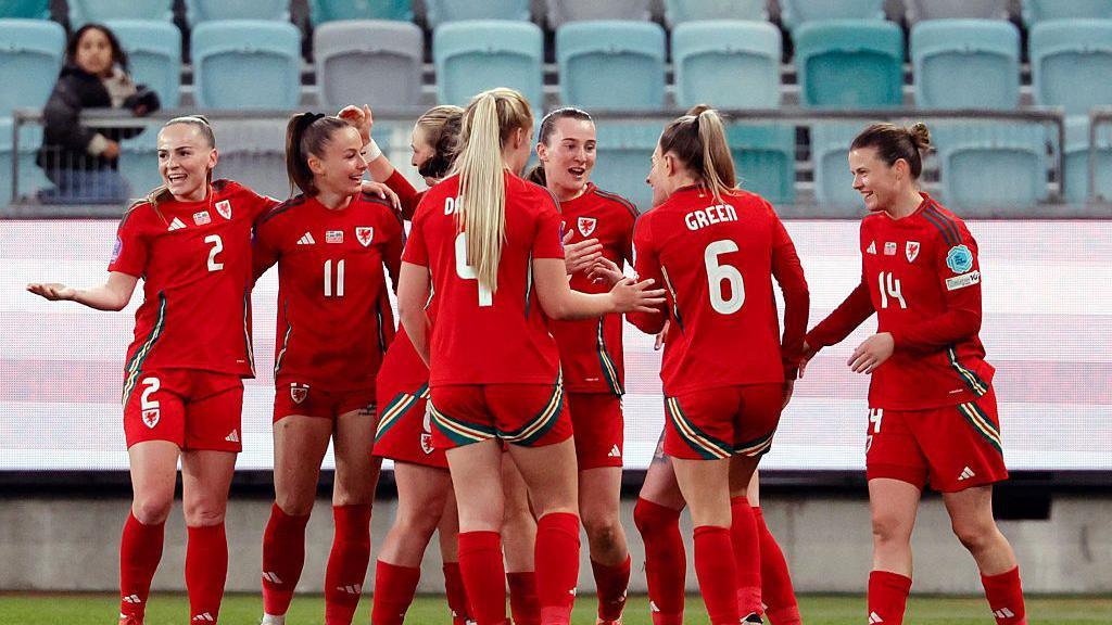 Welsh women's players wearing a red kit, including Josie Green and Lily Woodham, celebrate during the UEFA Women's Nations League football match against Sweden