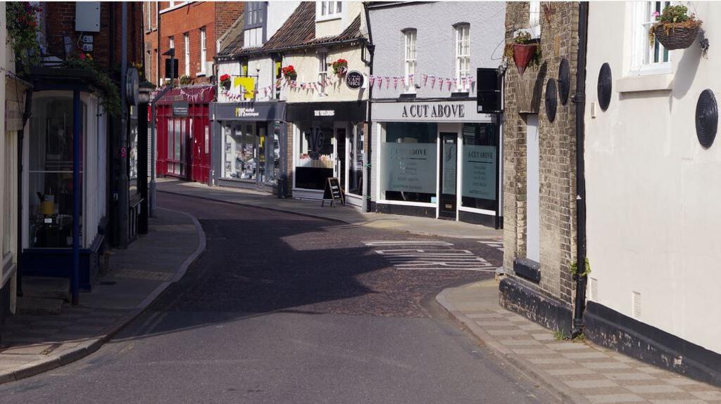 A winding street in North Walsham, with shop fronts and bunting above the windows.