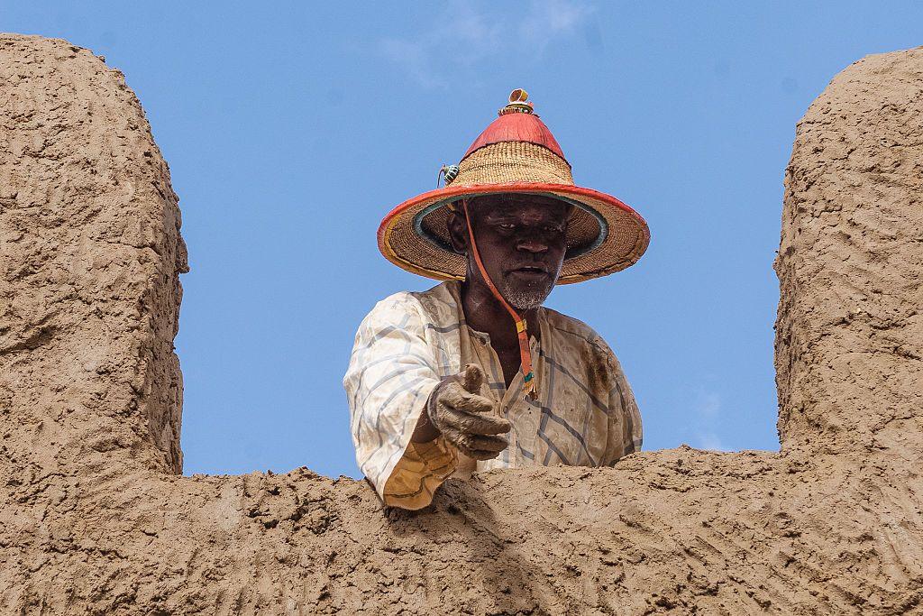 A man gestures for more building materials from a rooftop.