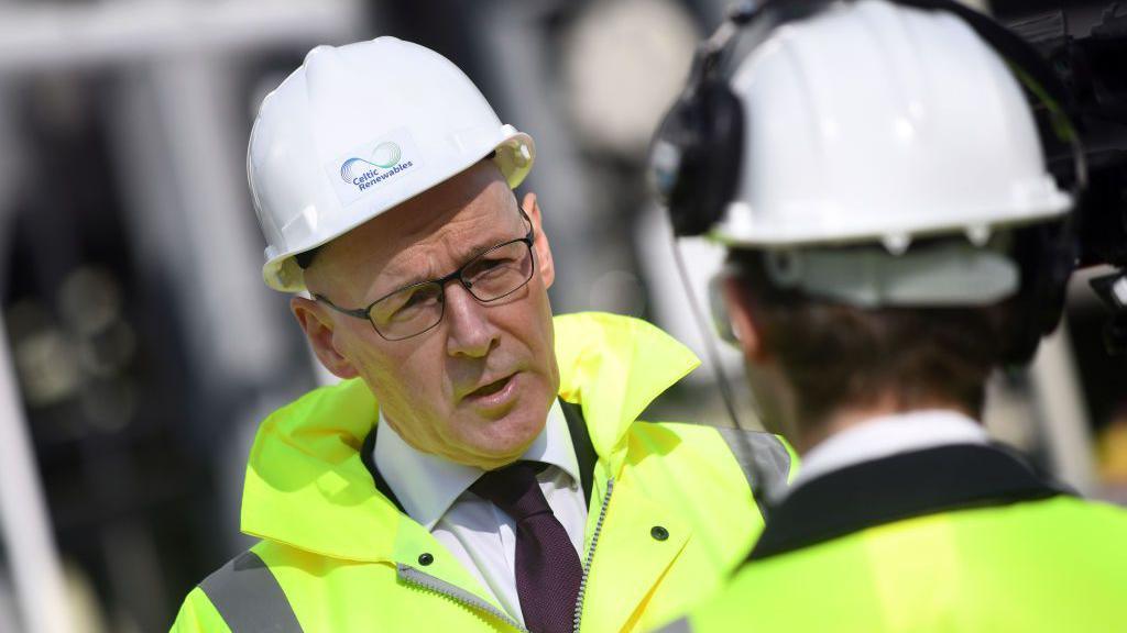 First minister John Swinney pictured on a visit to Grangemouth - he is wearing his customary glasses and purple tie, but also a white hard hat and a yellow hi-viz jacket