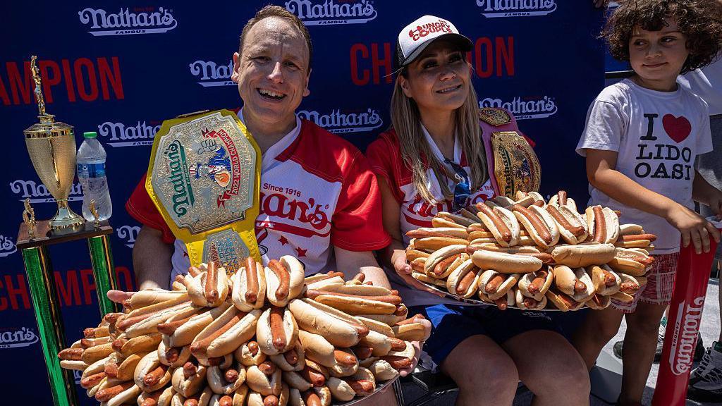 Joey Chestnut (L) and Miki Sudo (R) holding the equivalent number of hot dogs that they ate in 10 minutes.