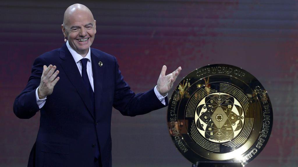 A smiling Gianni Infantino stands next to the Club World Cup trophy