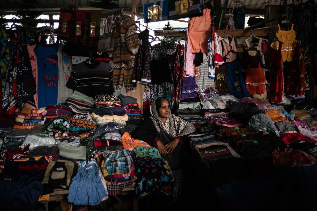 A female stall owner at a Sri Lankan market looks into the distance, surrounded by the clothes she is selling