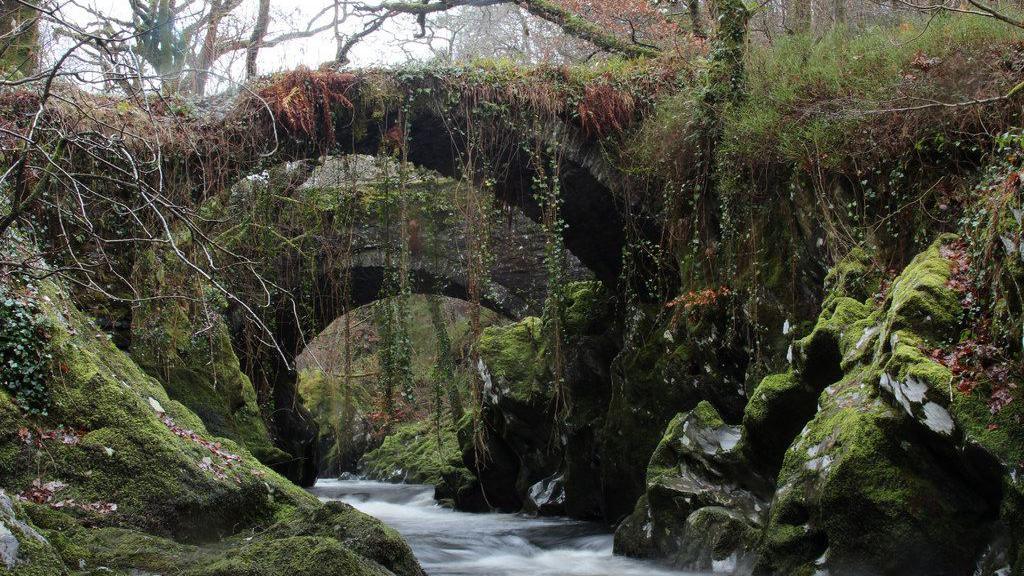 A single-span, 17th century packhorse bridge spans the banks of the River Machno.