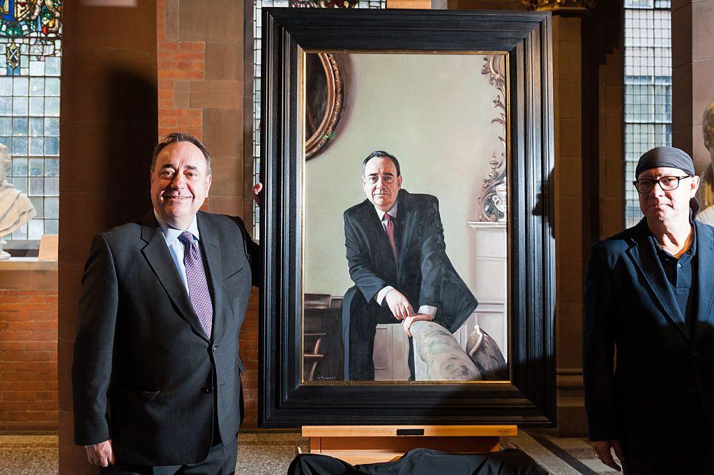 Alex Salmond and artist Gerard Burns unveil a painting of Salmond at the Scottish National Portrait Gallery. They are standing either side of the painting and Salmond is smiling.