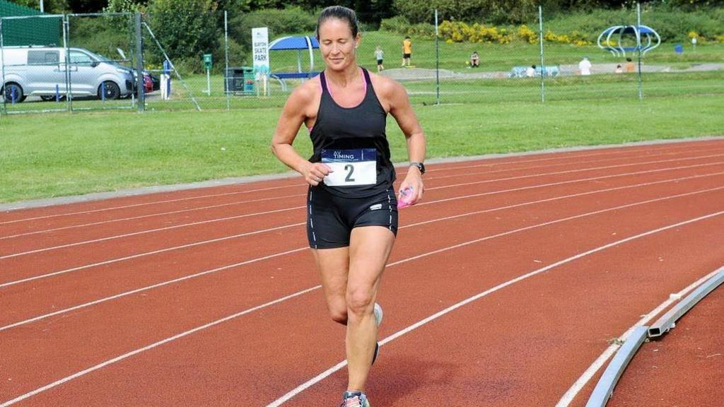 Harriet Lamb on a running track. She is wearing running gear and running trainers. 