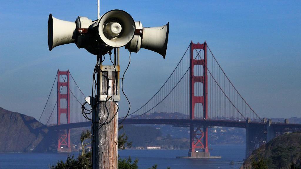 Aerial view of San Francisco's Outdoor Public Warning System. In the background is a waterway with a large red bridge standing in the water