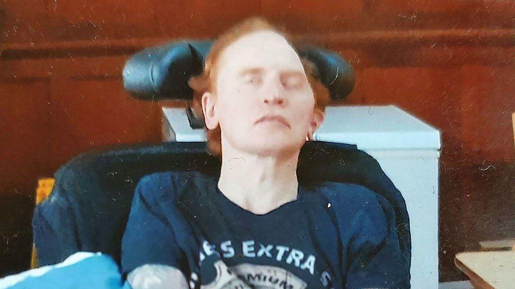 A man with ginger hair and his eyes closed in a wheelchair.