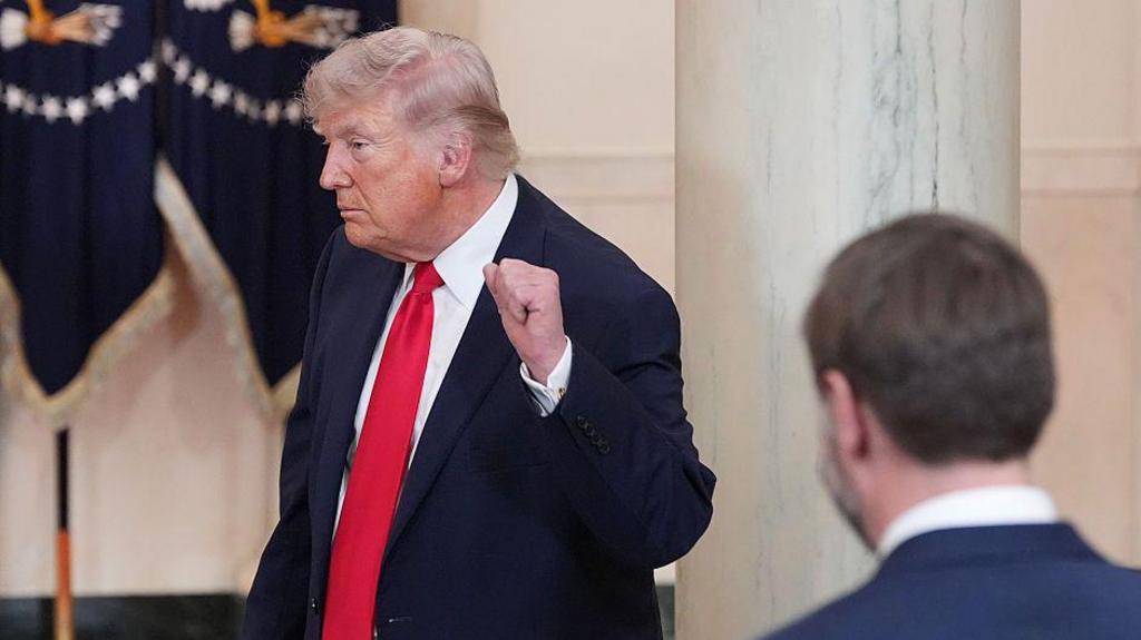 President Donald Trump, in a dark blue suit and red tie, fist bumps the air