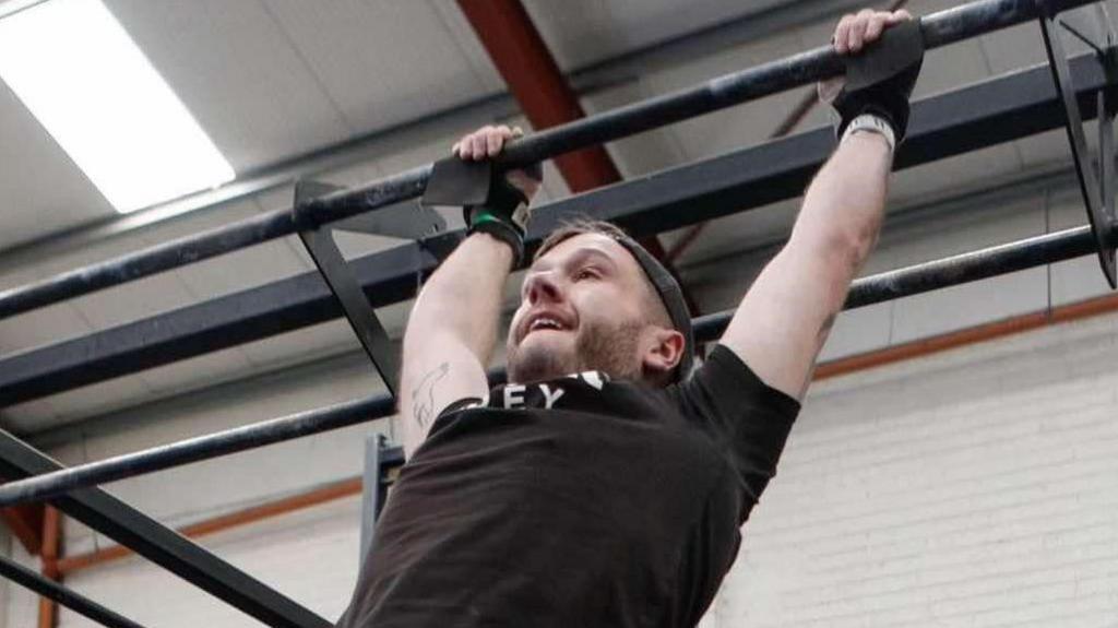 Isetyn Owen hangs from some exercise equipment during a gym workout.