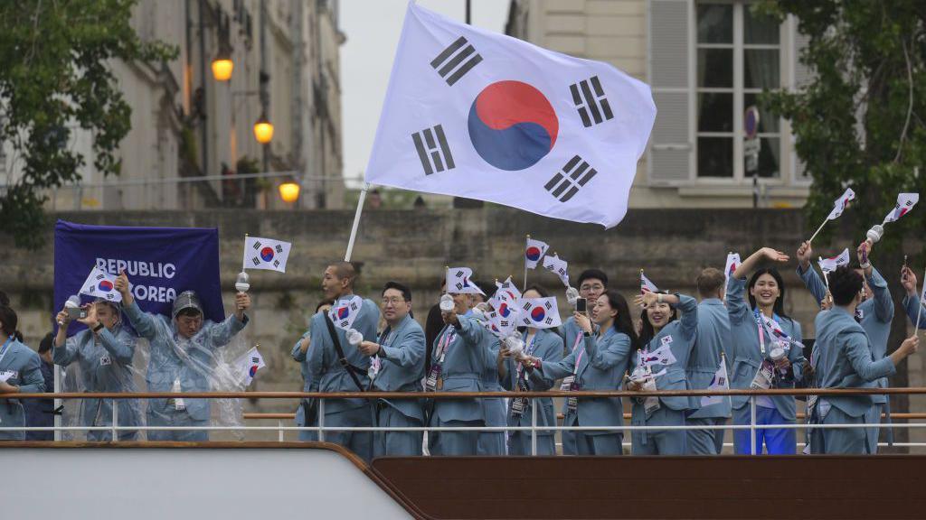 South Korean athletes wave flags while standing on a boat