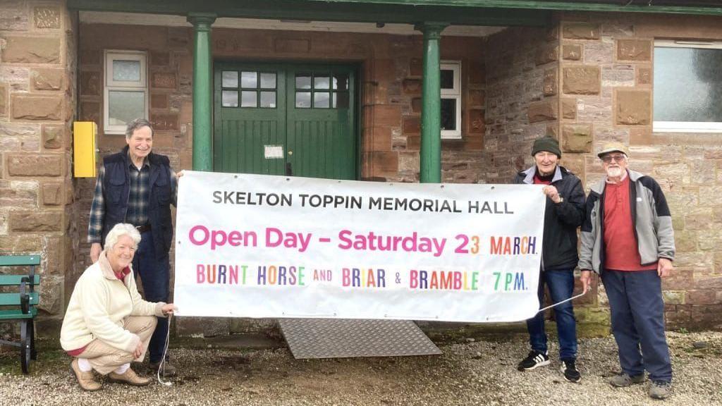 Christine Sealby, Bob Provoncha, William Pearson and Robert Towers standing outside the hall while holding up a banner to promote one of the many fundraising events that have taken place earlier this year.