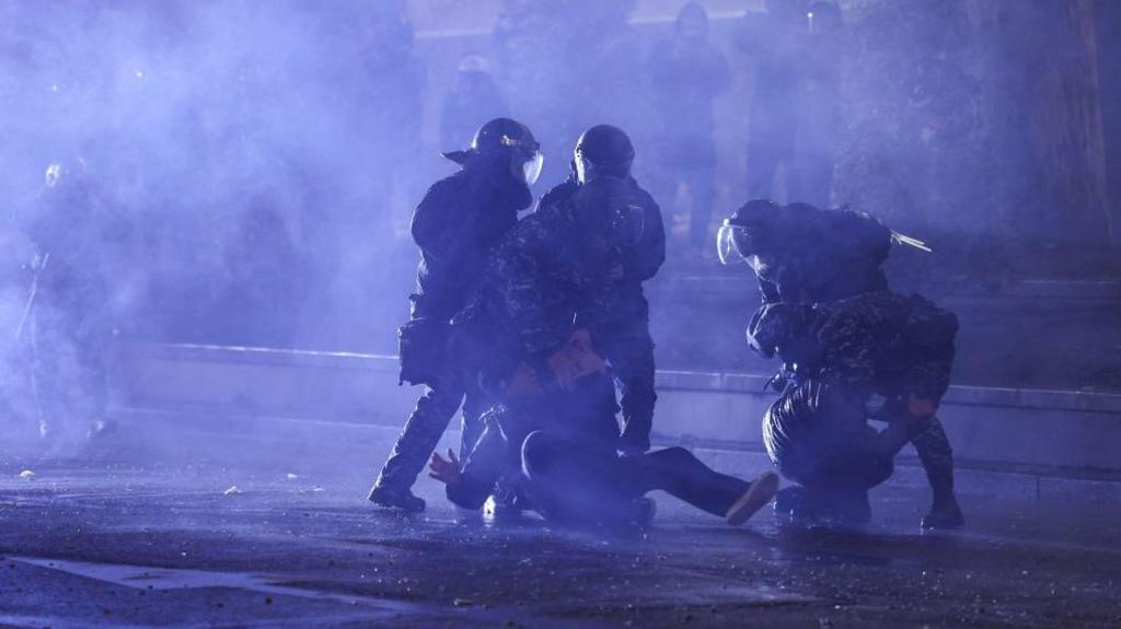 Police bundle a protester in Georgia to the ground on a darkened street in the capital