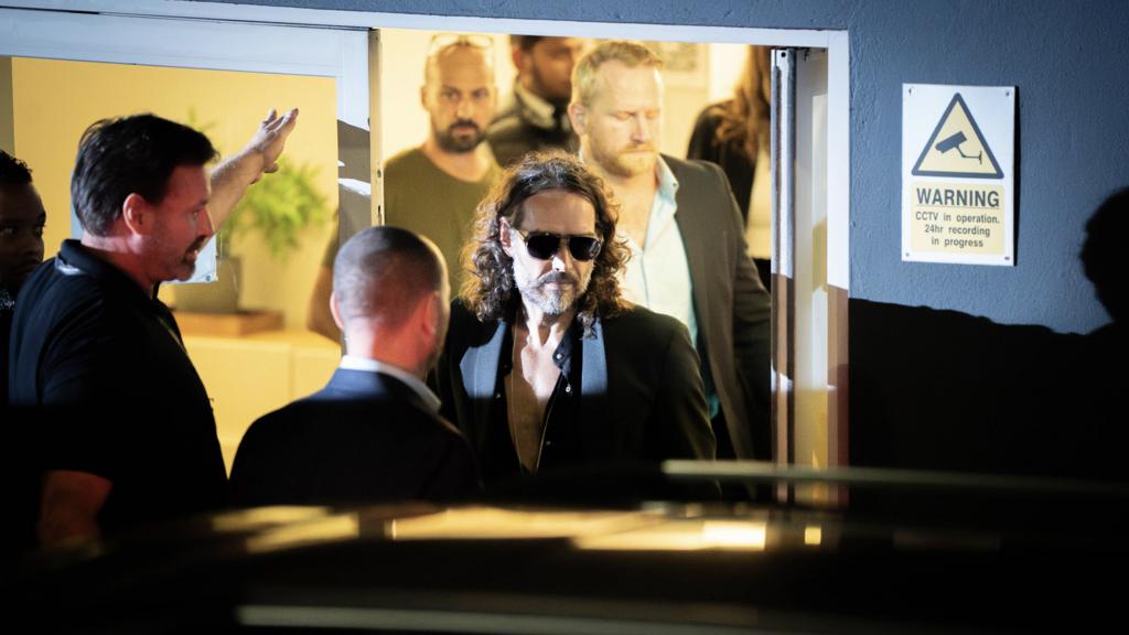 Russell Brand walking through a door