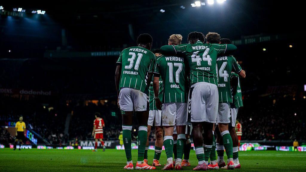 Werder Bremen have eight points from their last four Bundesliga matches. Werder Bremen players hug and celebrate their winning goal against Union Berlin. They are wearing green and white striped kits.