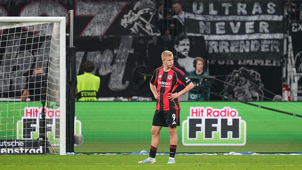 Jonathan Burkardt looks frustrated as Eintracht Frankfurt lose to RB Leipzig. He is wearing a red and black striped shirt with black shorts and socks.