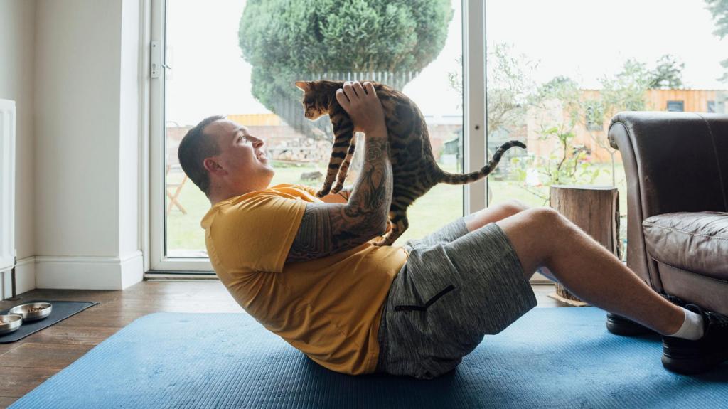 A man holds up his cat as he lies on the floor