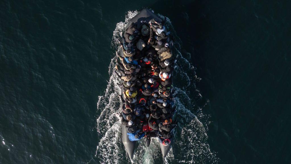 An aerial view of a smallboat carrying tens of people in the English Channel.