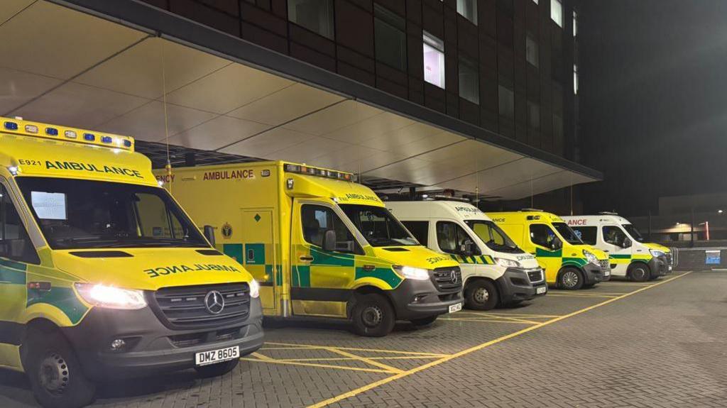 A number of ambulances lined up outside a hospital building. 