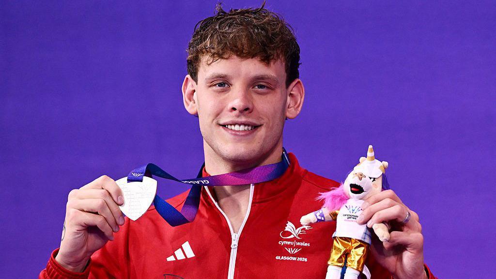 Matt Richards holding up his medal and Commonwealth Games mascot