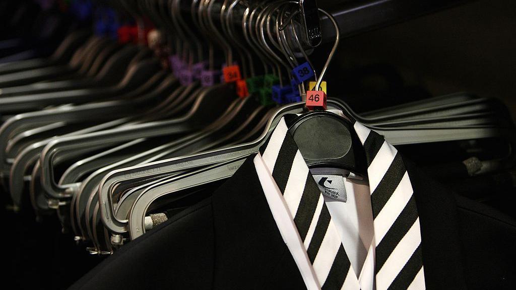 A rail with hangers, at the front is a black blazer, white shirt and black and white striped tie