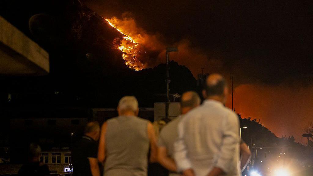 Bystanders watch as a wooden area is engulfed in flames during a raging wildfire near the town of Omis