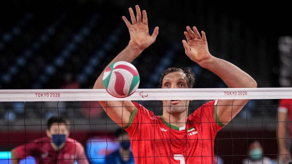 Morteza Mehrzadselakjani hitting a volleyball over a net. 