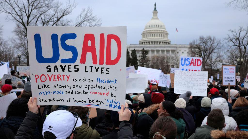 Protesters outside the Capitol in Washington, DC. A sign held by one protester reads: "USAID saves lives".
