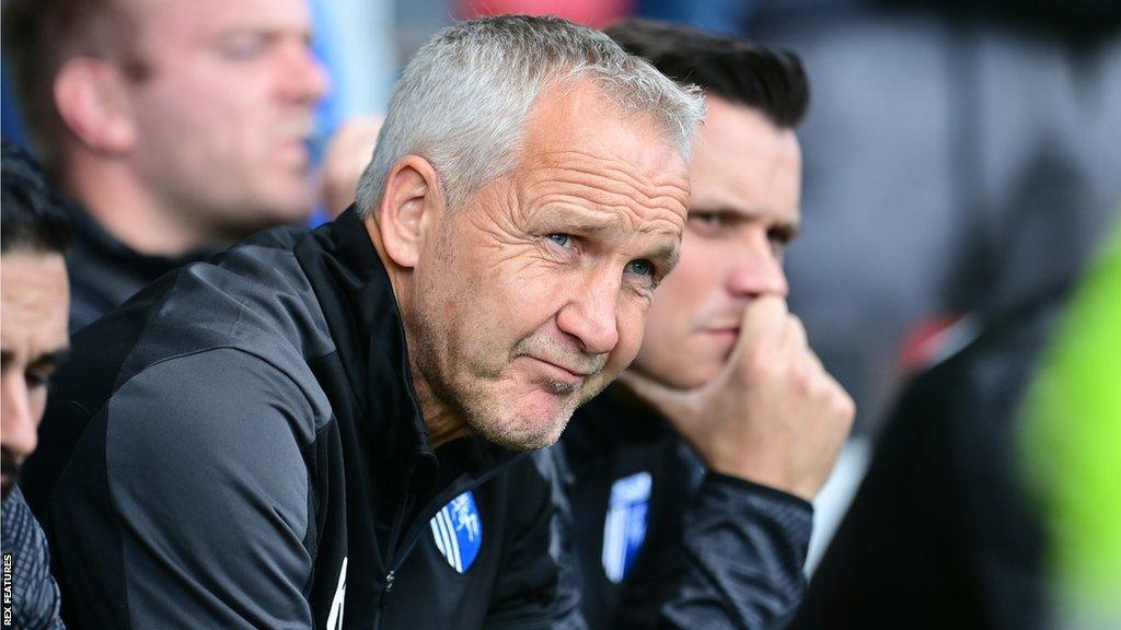 Keith Millen looks on to the pitch as he is sat in the dugout during a Gillingham game