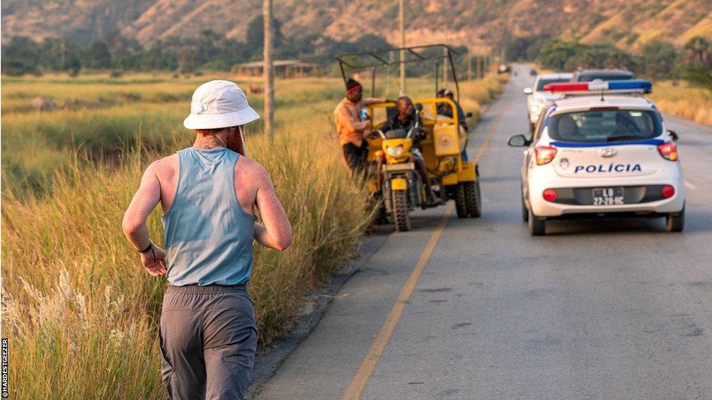 Russ Cook running along a road while receiving a police escort