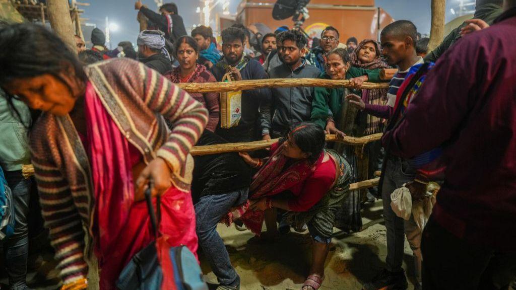 Crowd of pilgrims gather around a wooden fence while a woman in a pink suit attempts to climb between the fence.