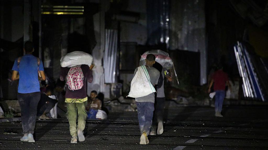 Palestinians carry food parcels from an aid distribution centre run by the Gaza Humanitarian Foundation (GHF) on Salah al-Din street, at the Nuseirat refugee camp, central Gaza (24 June 2025)
