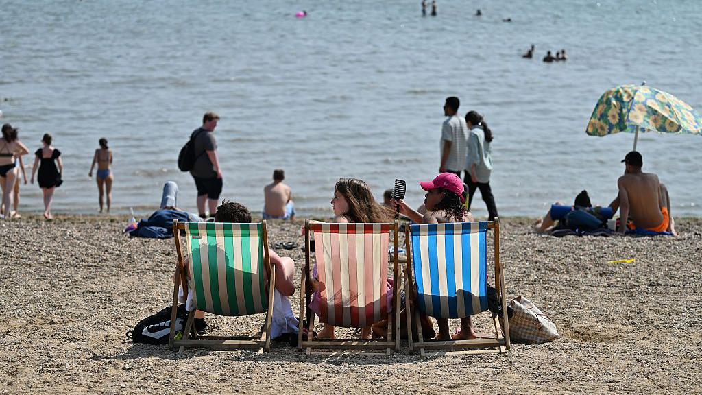 Three girls sit on deck chairs on a UK beach