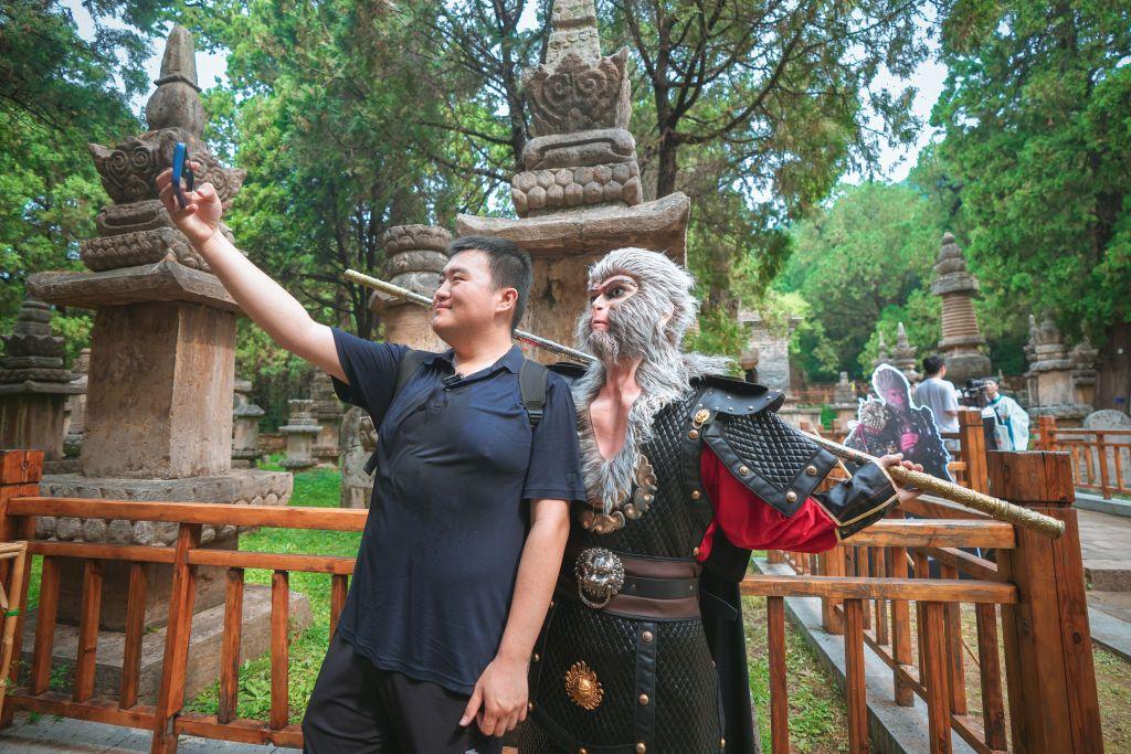 A tourist takes a selfie with a cast member dressed as Wukong, also known as Monkey King, at a temple in China