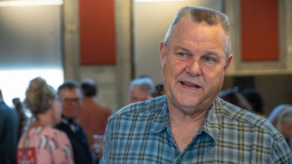 Jon Tester, wearing a flannel shirt, speaks to voters outside the frame as he campaigns for re-election