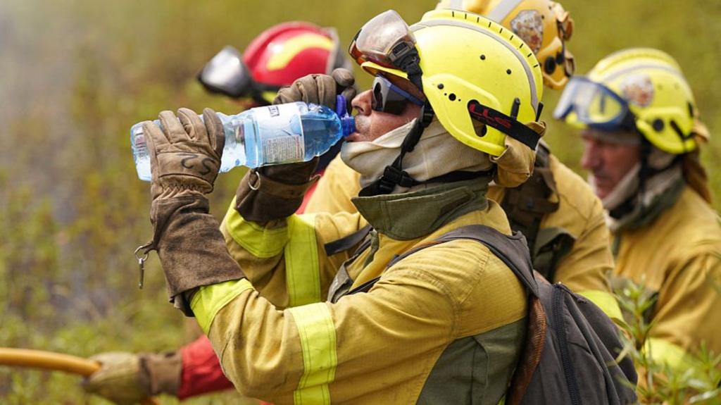 A firefighter drinks from a water bottle while tackling wildfires