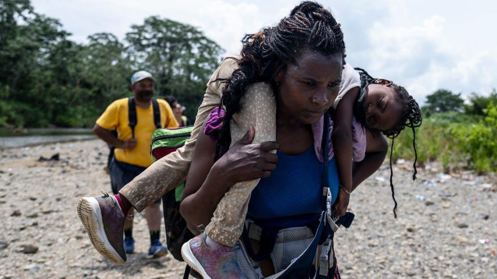 A migrant woman walks by the jungle carrying her daughter near Bajo Chiquito village, the first border control of the Darien Province in Panama, on September 22, 2023. 