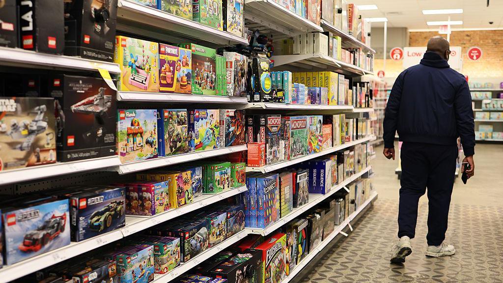 Man walks away wearing dark clothing in a store aisle lined with children's toys
