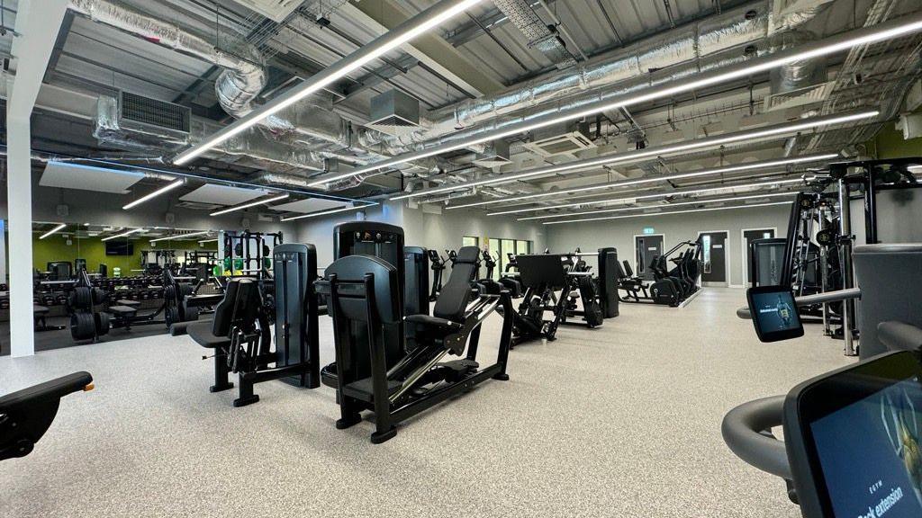 A gym featuring an array of exercise equipment, including cardio and resistance machinescise machines in a large, well-lit room, with mirrors lining the walls.