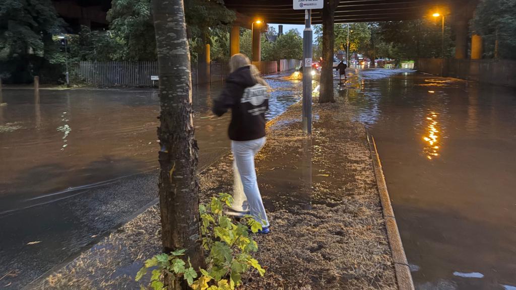 Woman walking in front of a flooded road underpass in Perry Barr, Birmingham